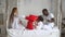 Happy mixed ethnicity family mom, african dad and little kid daughter having fun red pillow fight on bed. Young multi