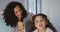 Happy mixed race mother and daughter brushing hair in bedroom