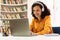 Happy mixed race woman in headphones studying online with laptop in library interior, watching webinar, copy space