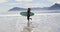 Happy mixed race woman running along beach by the sea carrying surfboard