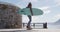 Happy mixed race woman skateboarding carrying surfboard on sunny promenade by the sea