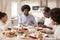 Happy mixed race young family of four eating Sunday dinner together, front view