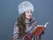 Happy modern woman in fur hat on cold blue reading book