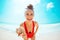 Happy modern woman in red swimwear on beach showing sea shell