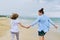 Happy mom and daughter running on the sea beach holding hands, back view