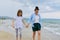 Happy mom and daughter walking on the sea beach holding hands