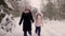 Happy mom mother and daughter join hand and walk through winter forest path pine tree woods snowfall