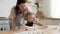 Happy mom teaching small child daughter rolling dough in kitchen