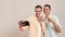 Happy moments with family. Young cheerful caucasian twin brothers showing thumb up while taking selfie on mobile phone