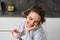 Happy mornings. Portrait of happy brunette woman, drinks cup of coffee in her kitchen and smiling, cozy and warm start