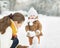 Happy mother and baby making snowman in winter park