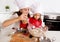 Happy mother baking with little daughter in apron and cook hat with flour dough at kitchen