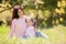 Happy mother and daughter in the autumn park. Beauty nature scene with family outdoor lifestyle. Happy family resting together on