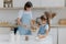 Happy mother and daughter bake together in kitchen, use different ingredients, wear aprons, stand against kitchen interior, girl