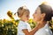 Happy mother with the daughter in the field with sunflowers having fun on a sunny summer day. Family value, unity, happiness, love