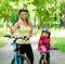 Happy mother and daughter having fun, riding a bicycle and showing thumbs up