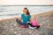 Happy mother and daughter sitting in lotus position on beach