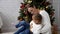 Happy mother having fun with her kid daughter next to Christmas tree