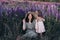 Happy mother and her little daughter in a field of lupins in summer. Mom holds her baby in arms