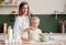 Happy mother and her little daughter kneading dough together at home in the kitchen