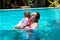 Happy mother with little baby daughter swims in the pool at summer holiday. Sunny day. Tropics. Infant watching around
