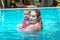 Happy mother with little baby daughter swims in the pool at summer holiday. Sunny day. Tropics. Infant watching to camera