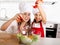 Happy mother and little daughter at home kitchen preparing paprika salad in apron and cook hat