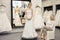Happy mother looking at young daughter dressed in wedding gown in bridal boutique