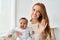 Happy mother waving hand holding funny baby daughter looking at camera at home.