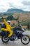 Happy motorcyclist traveler girl wearing yellow raincoat and sitting in a motorcycle saddle. Destination scene. Extreme travel