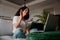 Happy multi-cultural female waving in online meeting while sitting on sofa in front of laptop