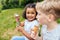 Happy multiethnic different age kids eating ice creams outdoor in summer. Curly positive hispanic girl enjoying blowing bulbs with