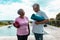 Happy multiracial senior friends holding yoga mats talking while standing at poolside against sky