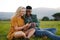 Happy multiracial young couple sitting and using mobile phone in field