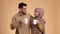 Happy Muslim Couple Drinking Coffee And Talking Hugging, Beige Background