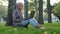Happy muslim islamic girl business woman in hijab sitting near tree on green grass in city park chatting with friends