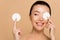 Happy naked asian girl removing makeup from face with cotton pads