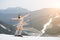 Happy naked female skier standing on the snowy slope of the mountain, rising hands up, wearing ski equipment