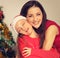 Happy natural smiling mother embrace her cute daughter with enjoying closed eyes in santa clause hat on Christmas green fur tree