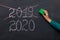 Happy new year 2020. Chalkboard with 2020, crossed 2019 and hand with sponge for washing