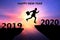 Happy New Year 2020 Silhouette. Young man jumps over a cliff in 2019 to a cliff in 2020