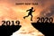 Happy New Year 2020 Silhouette. Young man jumps over a cliff in 2019 to a cliff in 2020