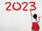 Happy new year 2023 Little girl holding a paint brush painting on a white wall background,