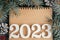 Happy New Year 2023. White numbers 2023 lying on folded notebook with Christmas tree branches and pine cones, copy space