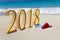 Happy new year card. Two New Year`s caps of Santa Claus on beach and inscription 2018 in the sand