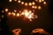 Happy New Year. Glowing sparklers in couple hands on background of golden christmas tree lights, family celebrating in dark