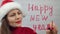 Happy New Year. Santa girl writes lipstick on glass words happy new year. Beautiful girl in hat sending a message.