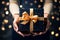 Happy New Year! A woman hands present an elegant present gift box with golden ribbon , background with gold bokeh, top view