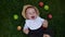 Happy Newborn child in summer panama hat Fall down laying on grass barefoot in Summer Sunny Day with Fresh Fruits Apples