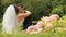 Happy newlywed bride and groom kissing, in blossoming green summer park. Elegant groom holds his gorgeous bride